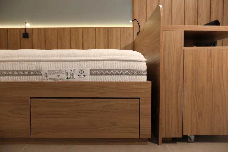 Cama sobre base de marcenaria com gavetão, ao lado de painel ripado de madeira.