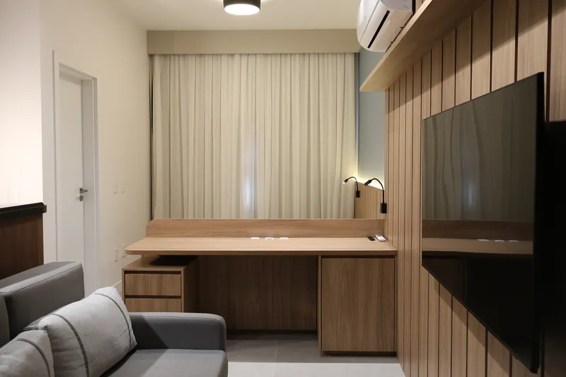 Sala e dormitório integrados do studio, com bancada de trabalho, televisão e sofá.