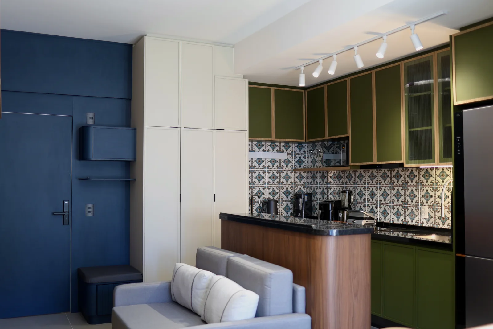 Cozinha do Studio LeM com marcenaria verde-oliva, azulejo estampado e porta azul.